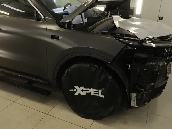 Автомобиль с разобранным передним бампером и защитным чехлом XPEL на колесе в детейлинг-центре