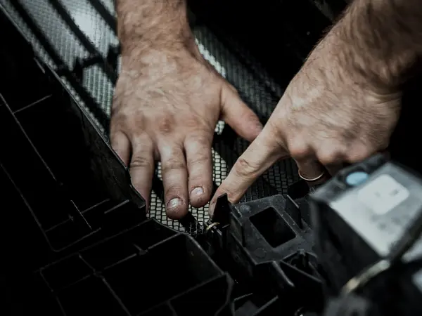 Руки мастера крепят защитную сетку к внутренней части бампера перед оклейкой плёнкой