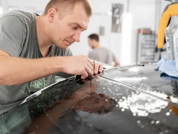 Мастер подрезает антихром-плёнку на кузове автомобиля с мыльным раствором