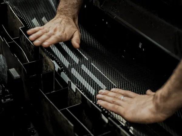 Мастер устанавливает чёрную сетку в решётку радиатора перед покраской хрома