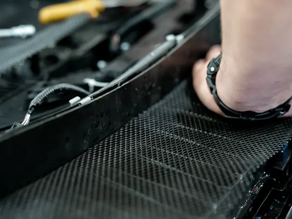 Мастер закрепляет сетку на внутренней стороне бампера, вид сверху на рабочий процесс