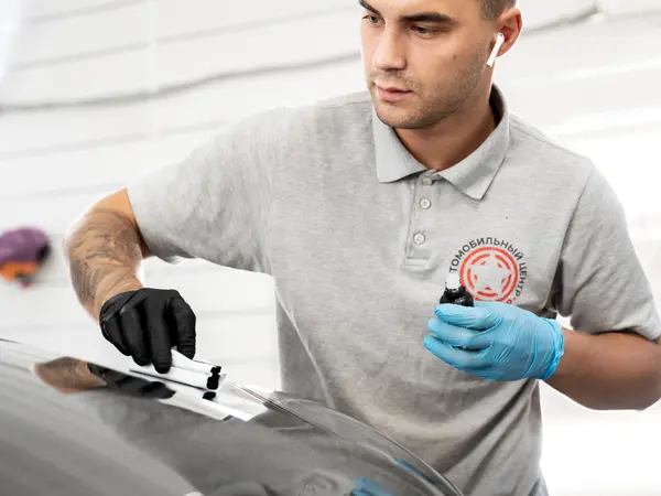 Мастер наносит керамический состав аппликатором на крыло серого Porsche Cayenne поверх плёнки