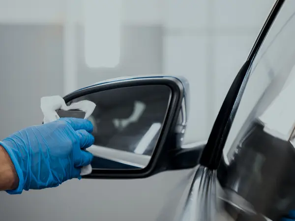 Мастер в синей перчатке протирает боковое зеркало автомобиля после нанесения жидкого стекла