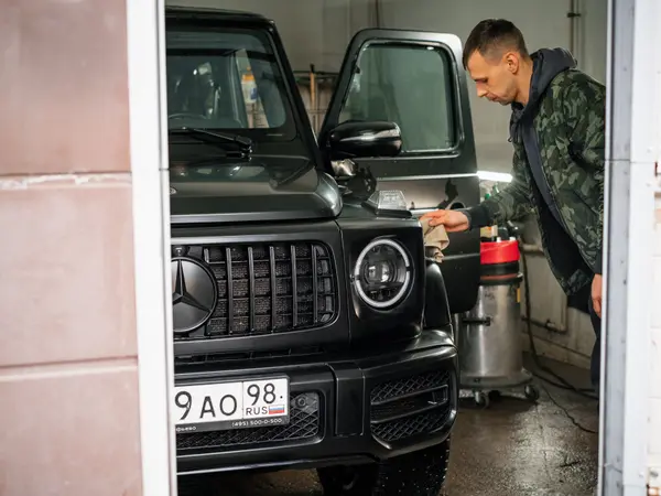 Мастер протирает фару чёрного Mercedes-Benz G-Class на мойке детейлинг-центра