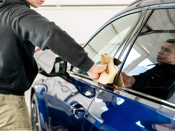 Мастер протирает стекло синего автомобиля замшевой салфеткой после мойки