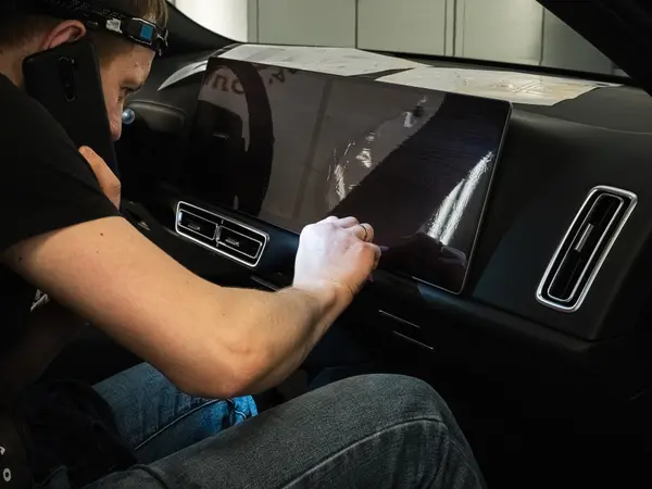 Мастер оклеивает защитной плёнкой мультимедийный экран в салоне автомобиля