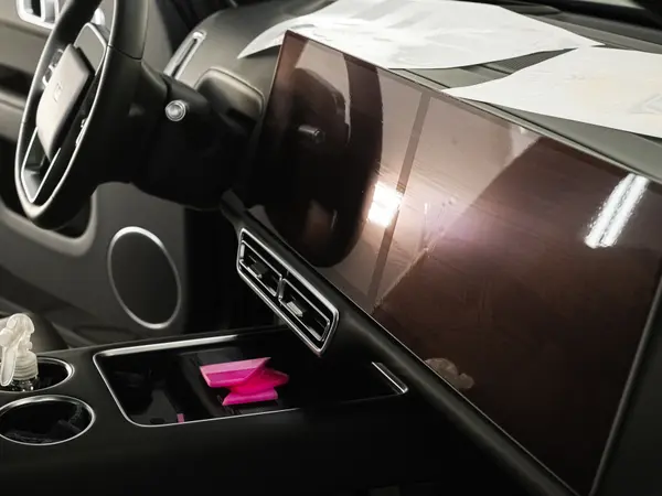 Центральная консоль автомобиля с большим экраном после оклейки плёнкой, розовый ракель рядом