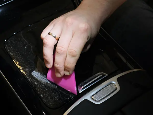 Рука мастера разглаживает защитную плёнку розовым ракелем на глянцевой панели консоли