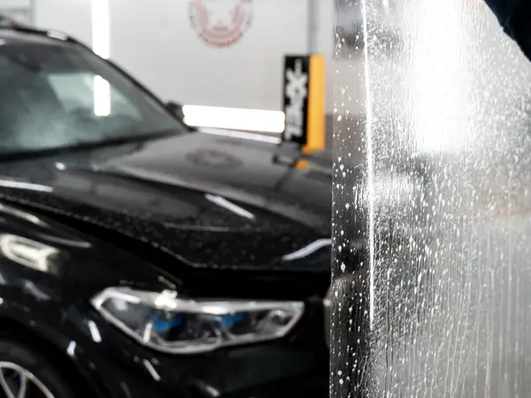 Раскатка защитной бронеплёнки на капоте чёрного BMW — крупный план с мыльным раствором