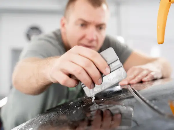 Мастер выгоняет воду ракелем из-под защитной плёнки на крыше автомобиля крупным планом