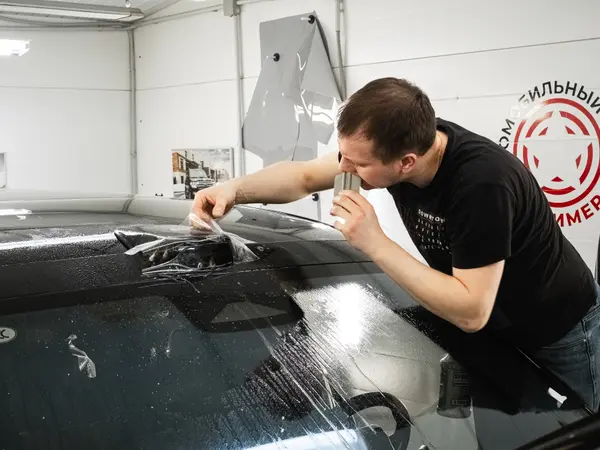 Мастер разглаживает защитную плёнку ракелем на крыше автомобиля в цехе АЦ Полимер