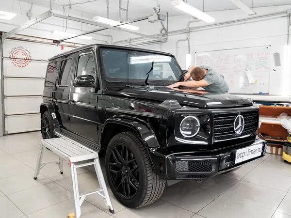 Мастер оклеивает капот чёрного Mercedes-Benz G-Class защитной плёнкой в детейлинг-центре