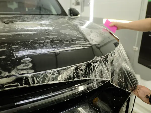 Нанесение защитной плёнки на капот чёрного автомобиля — разглаживание розовым ракелем с мыльным раствором