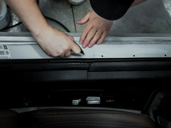 Мастер подрезает защитную плёнку на пороге автомобиля ножом, вид сверху крупным планом