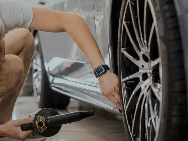 Мастер продувает турбосушкой зону порога серебристого автомобиля перед оклейкой плёнкой
