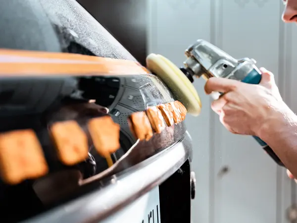 Мастер полирует задний бампер автомобиля роторной полировальной машинкой крупным планом