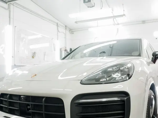 Белый Porsche Cayenne в детейлинг-боксе перед полировкой, вид на капот и фару