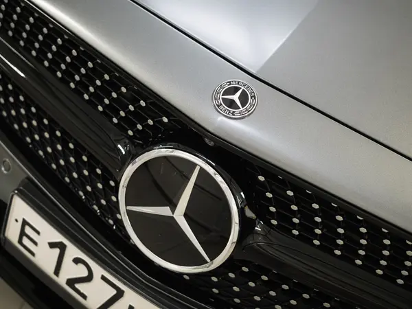 Эмблема Mercedes-Benz на решётке радиатора серебристого автомобиля после полировки царапин