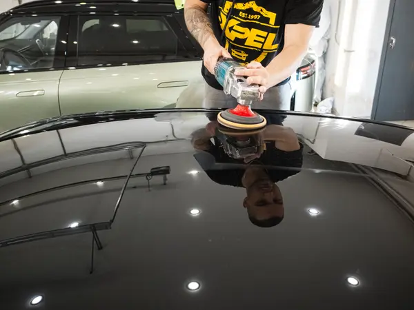 Полировка крыши чёрного автомобиля — зеркальный блеск отражает потолочные светильники