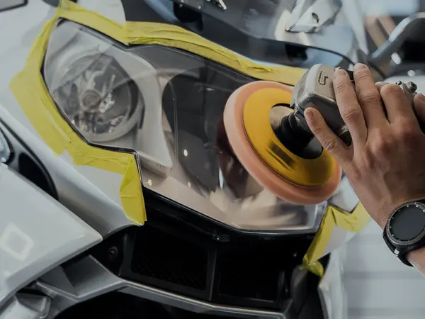 Мастер полирует фару мотоцикла BMW оранжевым полировальным кругом, защитная малярная лента по контуру