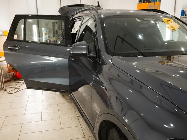 Тёмный BMW X7 с открытой дверью в боксе после глубокой полировки кузова