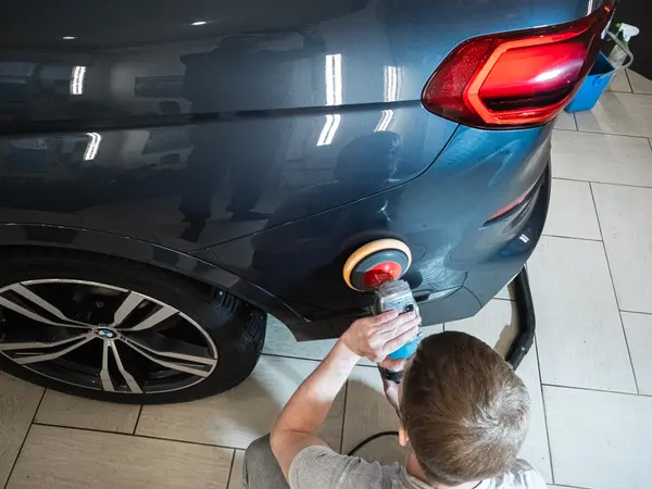 Мастер полирует задний бампер тёмно-синего BMW роторной машинкой, вид сверху