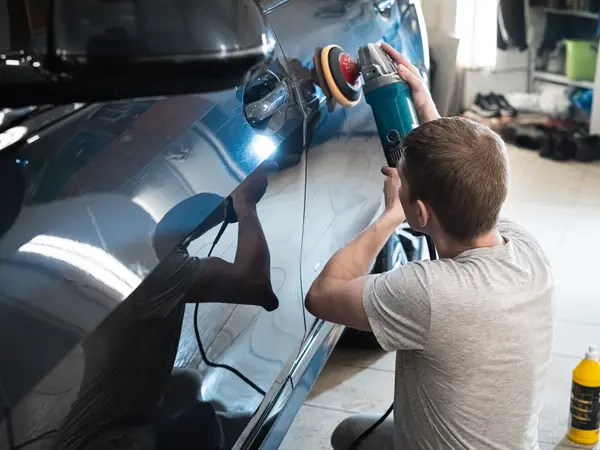 Мастер выполняет глубокую полировку двери тёмно-синего BMW с подсветкой дефектов