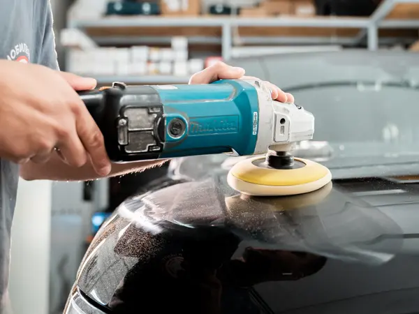 Мастер полирует капот тёмного автомобиля роторной машинкой Makita с поролоновым кругом