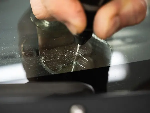 Мастер вводит полимер инжектором в скол на лобовом стекле, крупный план ремонта