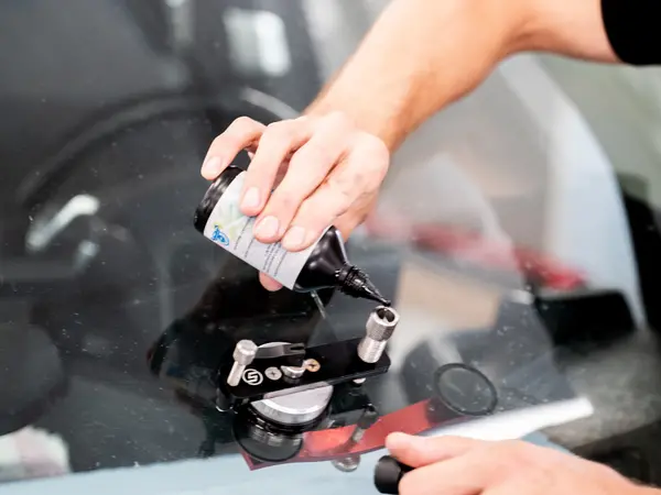 Мастер заливает полимерную смолу в инжектор на лобовом стекле автомобиля