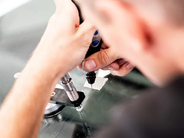 Мастер работает дремелем и инжектором над лобовым стеклом, вид сверху крупным планом