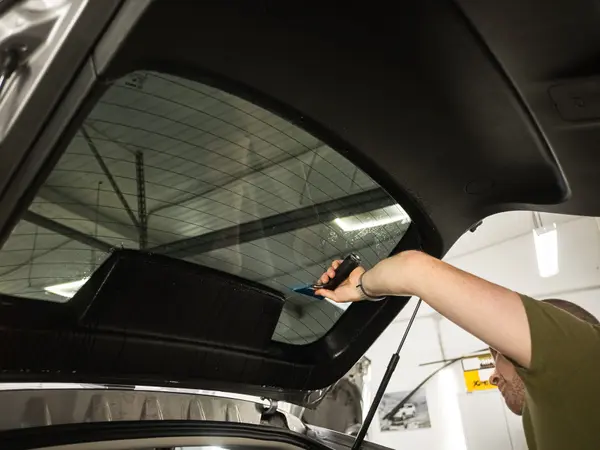 Установщик подрезает атермальную плёнку на заднем стекле автомобиля через открытый багажник
