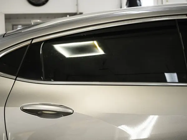 Тонированное заднее боковое стекло серебристого автомобиля крупным планом в детейлинг-центре