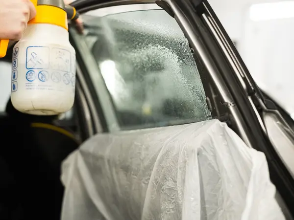Нанесение мыльного раствора из пульверизатора на боковое стекло перед установкой тонировки